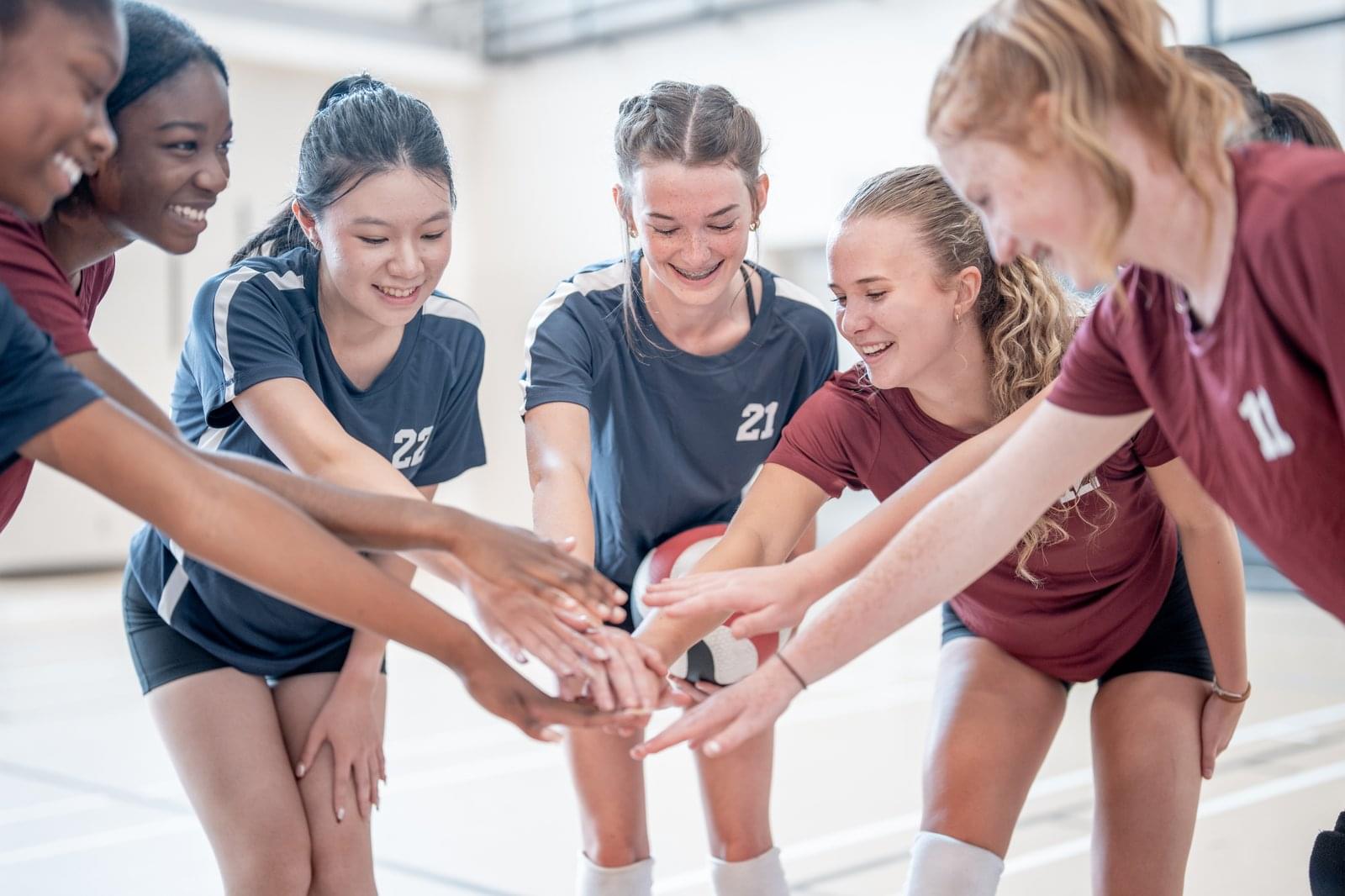 Diverse all-female team huddle with hands together over a volleyball