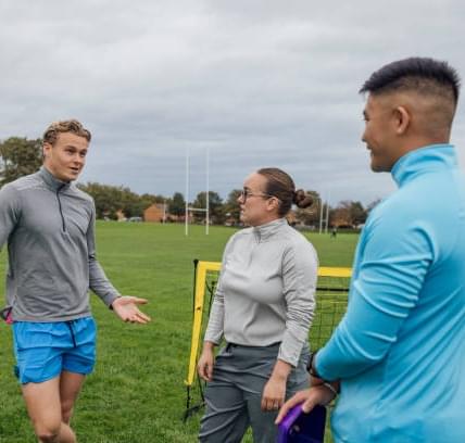 Rugby coach working with two athletes on the pitch