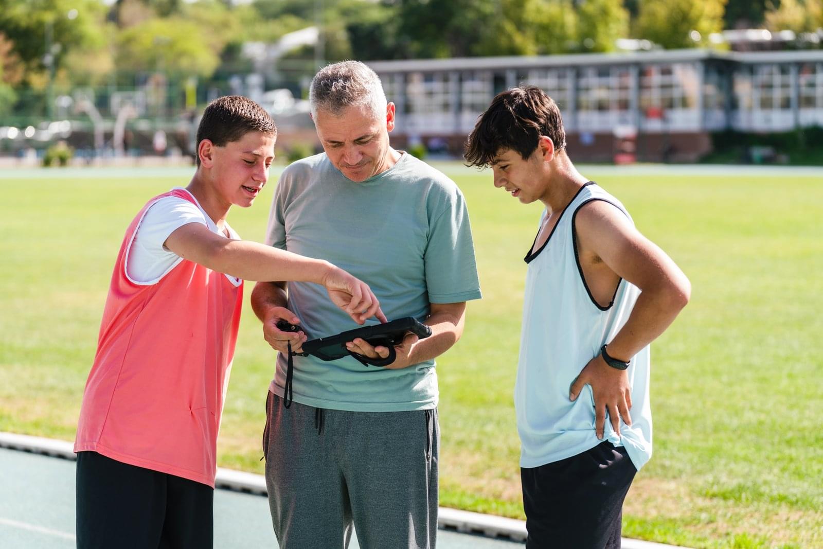 Coach showing two young athletes data on a tablet at the trackside